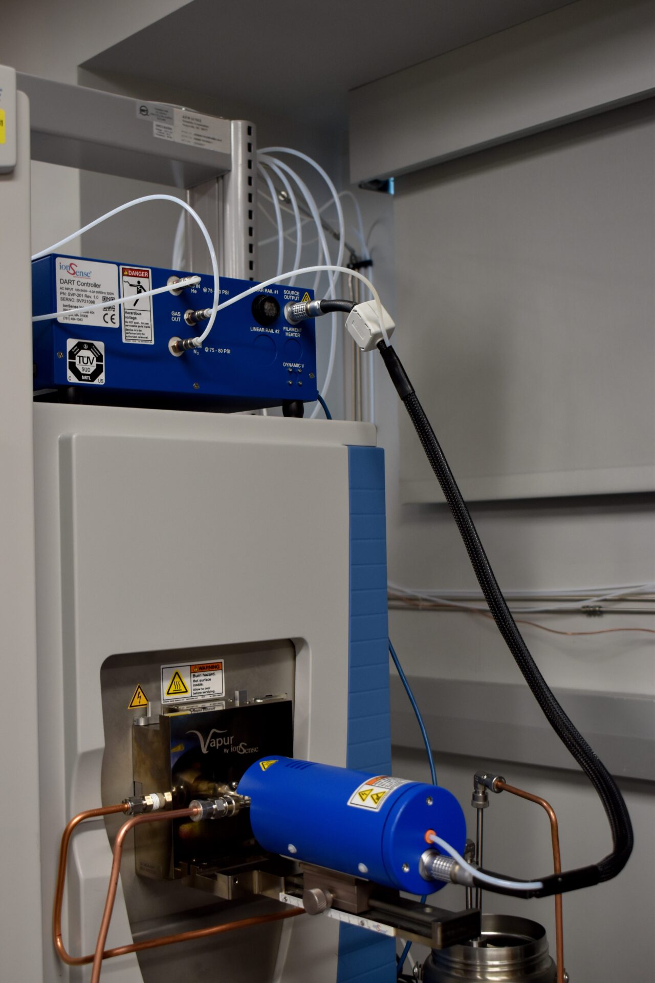Laboratory equipment with blue and gray components, including tubes and a heat sink. Various warning labels are visible.