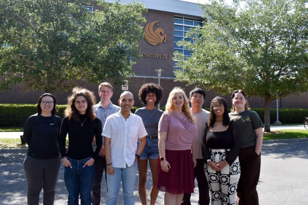A group of ten people stands outside in front of a building with the UCF logo and the word "Research" visible on the wall.