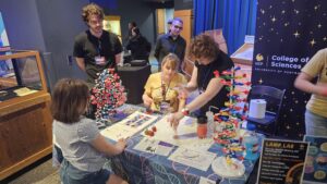 A group of people, including children and adults, interact with molecular models and science displays at a University of Central Florida College of Sciences booth.