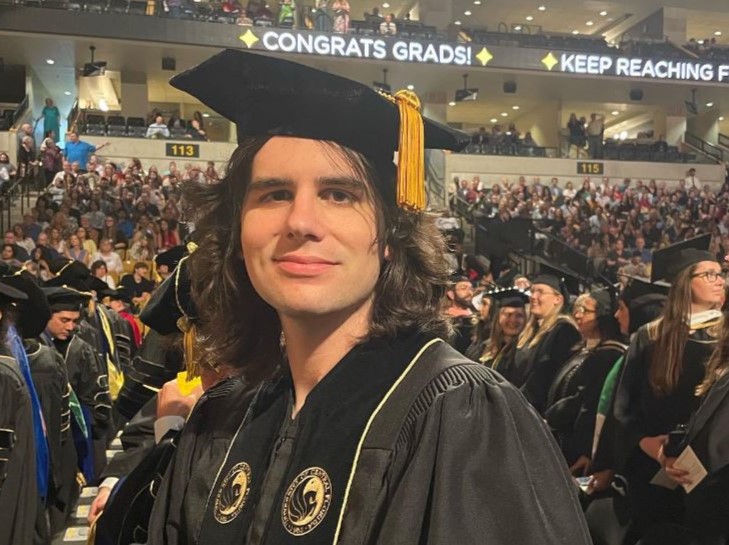 A man in a graduation cap and gown standing in front of a crowd.