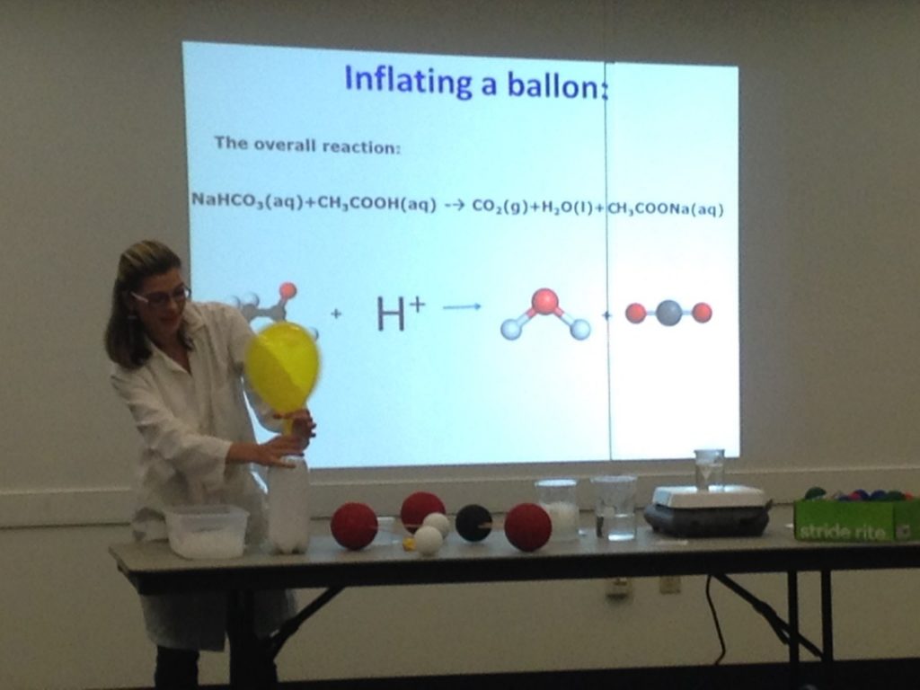 Science teacher demonstrating a chemical reaction to inflate a balloon during a classroom experiment.