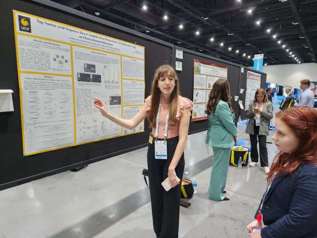 A presenter explaining her research poster to an attendee at a scientific conference.