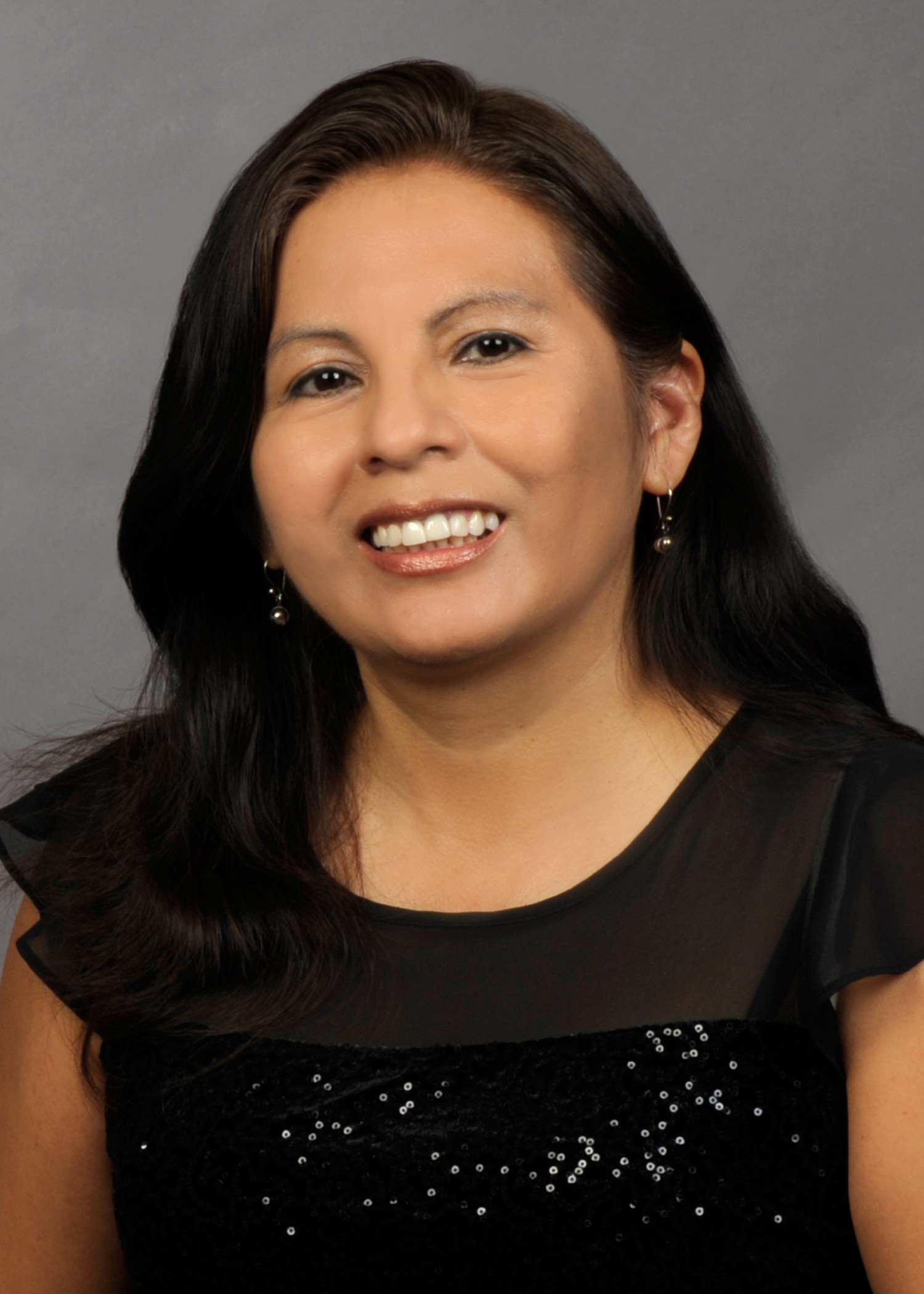 Portrait of a smiling woman with long dark hair, wearing a black sequined top and earrings.